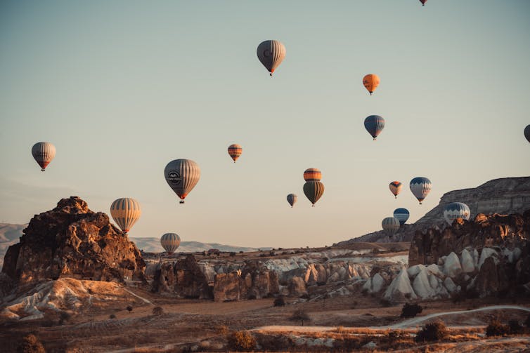 A rocky desert scene with several colourful hot air balloons in the sky