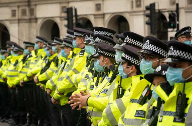 A group of Met Police officers in hi-vis jackets and face masks, standing side by side in a line