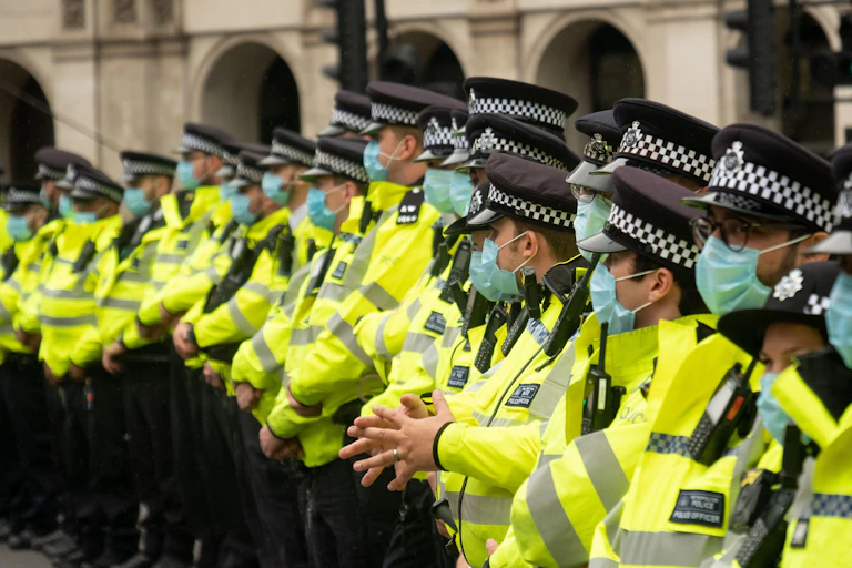 A group of Met Police officers in hi-vis jackets and face masks, standing side by side in a line