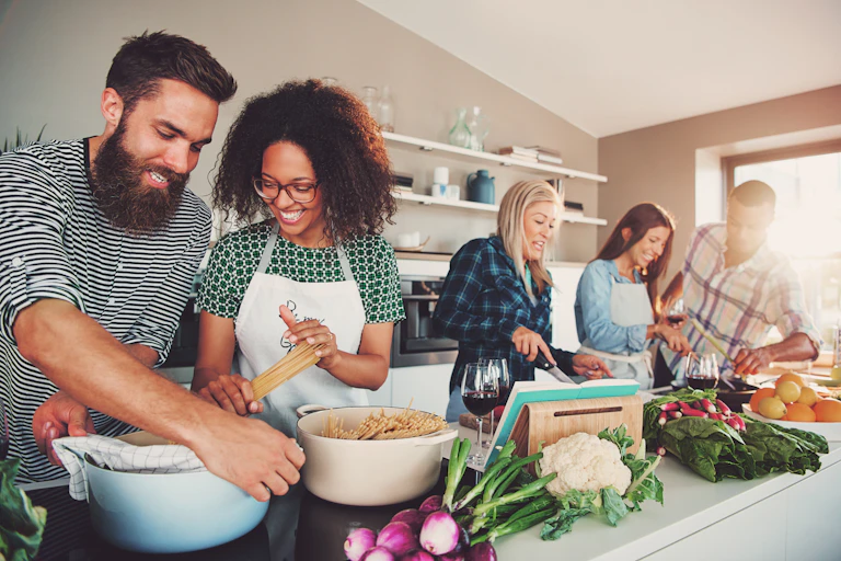 A group of five people in their 20s or 30s cook together in a kitchen.