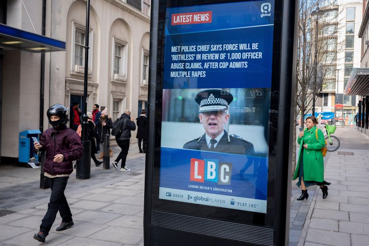 A digital advertising board on a London sidewalk with a photo of Met Commissioner Mark Rowley and a headline about the review of 1,000 officer abuse claims