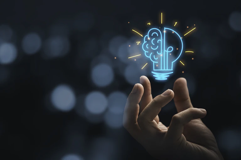 Hand holding drawing virtual lightbulb with brain on bokeh background