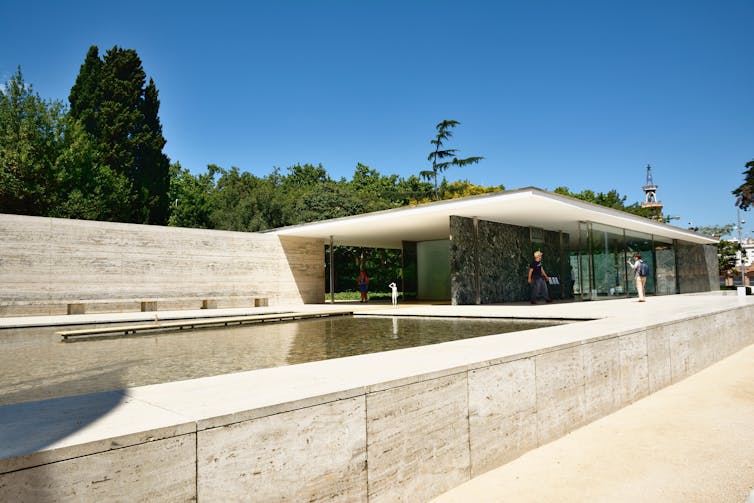 A smooth low-rise flat-roofed concrete building with a shallow reflecting pool.
