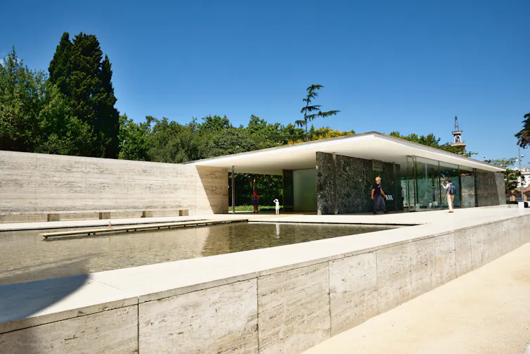 A smooth low-rise flat-roofed concrete building with a shallow reflecting pool.