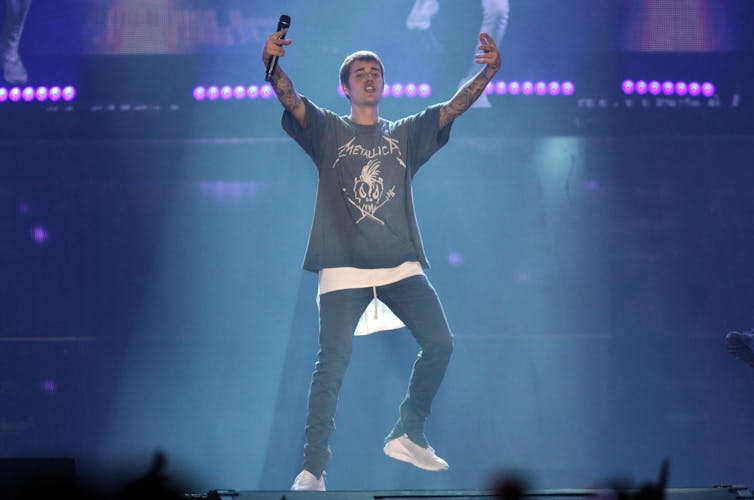 Justin Bieber standing on stage, holding his arms aloft.