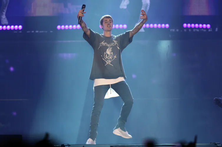 Justin Bieber standing on stage, holding his arms aloft.