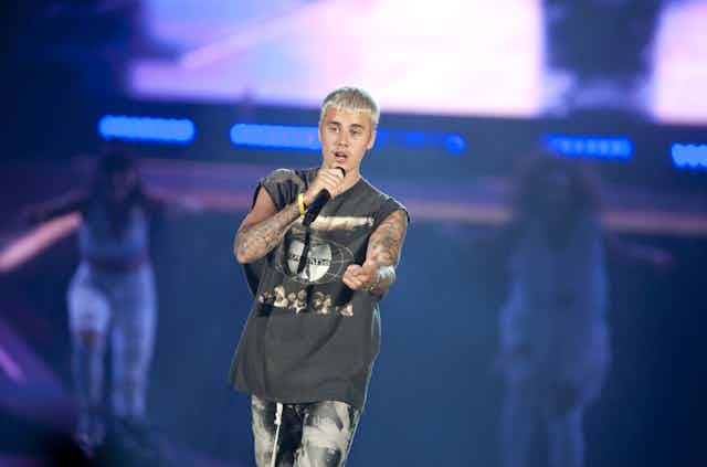 Justin Bieber performing on stage with cropped blonde hair, wearing a Wu Tang Clan t-shirt. 