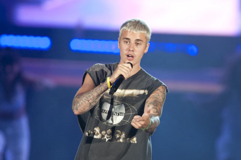 Justin Bieber performing on stage with cropped blonde hair, wearing a Wu Tang Clan t-shirt.