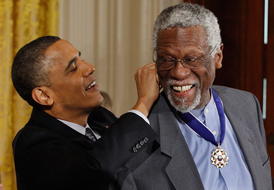 A black man dressed in a business suit is tying a ribbon around the neck of another black man.