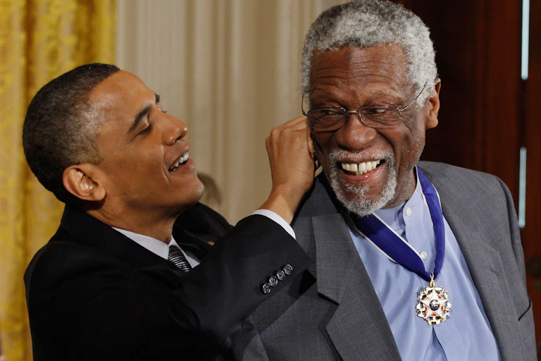 A black man dressed in a business suit is tying a ribbon around the neck of another black man.