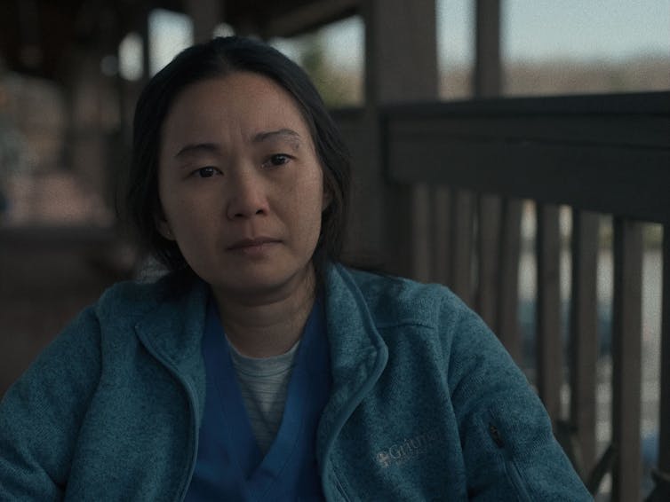 Hong Chau wears a blue jacket and sits on a balcony.