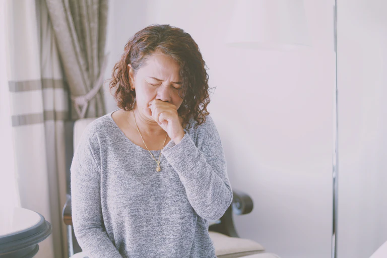 Woman in grey shirt coughing into hand