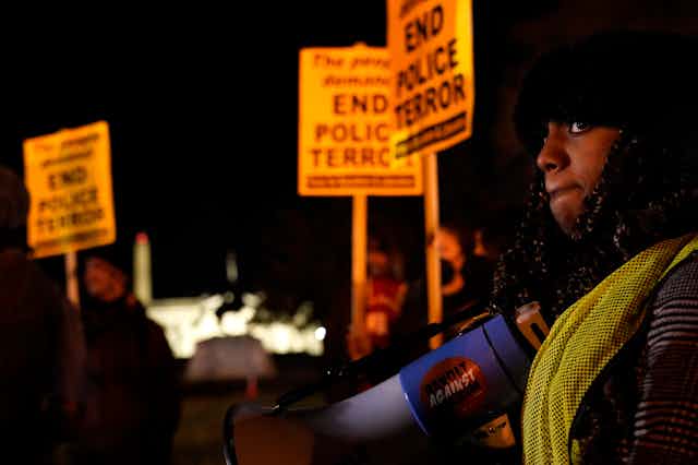 A woman holds a bullhorn and people next to her carry signs that read End Police Terror.