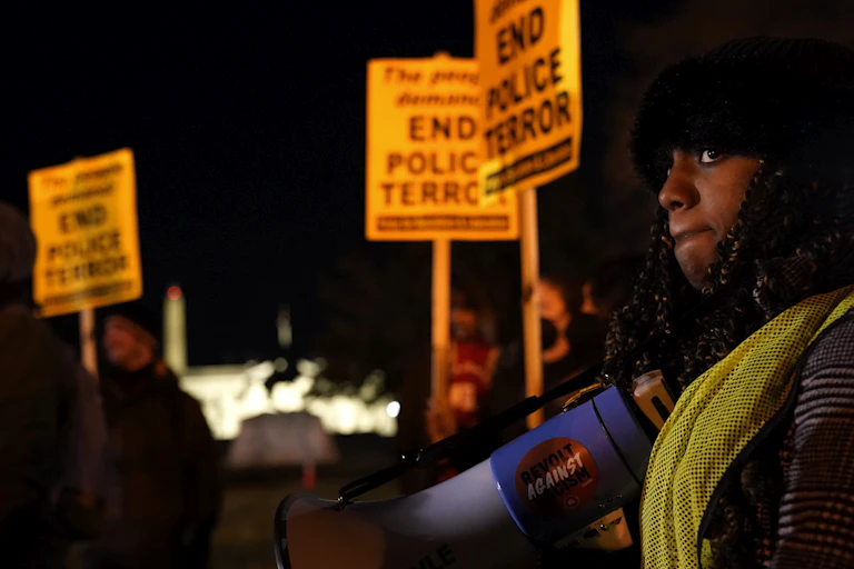 A woman holds a bullhorn and people next to her carry signs that read End Police Terror.