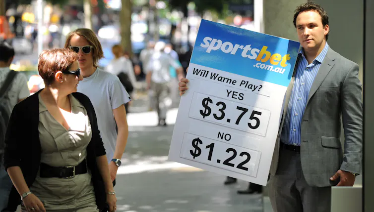 Man in suit holds sign advertising betting odds to passersby.