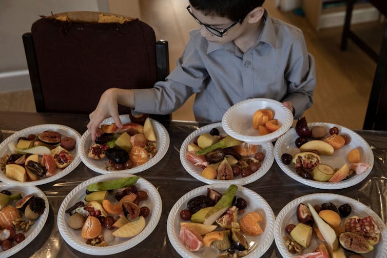 A boy arranges plates full of fruit on a table.