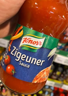 A hand holding a glass bottle of red sauce that says'Zigeuner Sauce' on the label