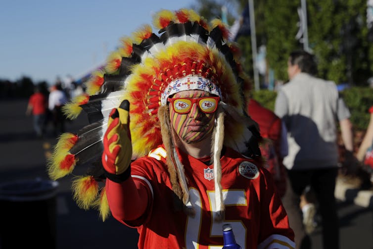 A sports fan in a red jersey wearing a Native American-style headdress and red, black and yellow face paint