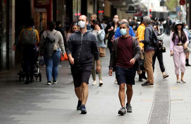 Two men in surgical masks walk down a busy Sydney street