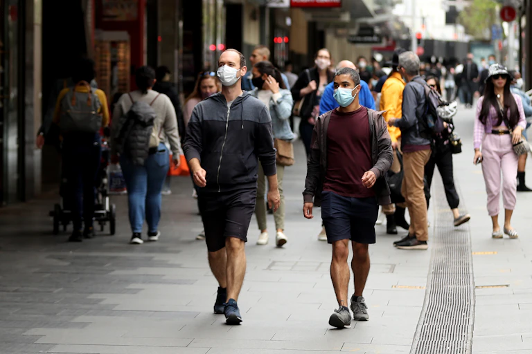 Two men in surgical masks walk down a busy Sydney street