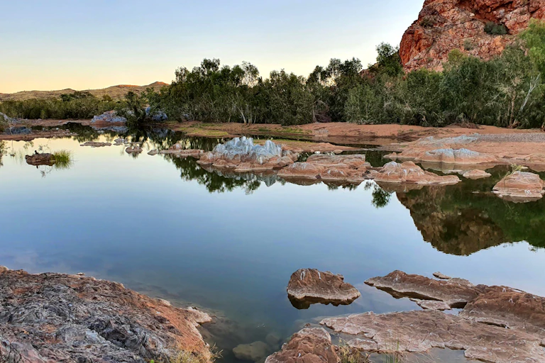 A photo of a pool of water surrounded by angular outcrops of red and grey rock.