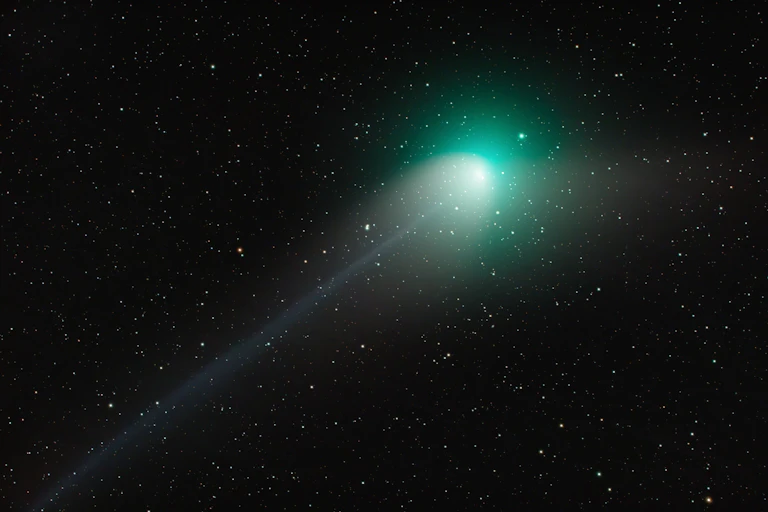 A dark star field with a bright green light and a faint white trail behind it shooting diagonally to the right