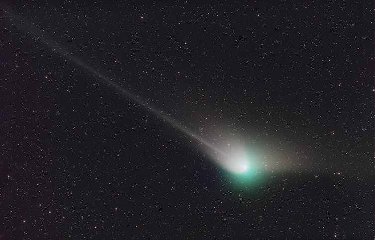 A dark star field with a bright green and white light on the lower-right corner, with two white streaks coming out of it in different directions