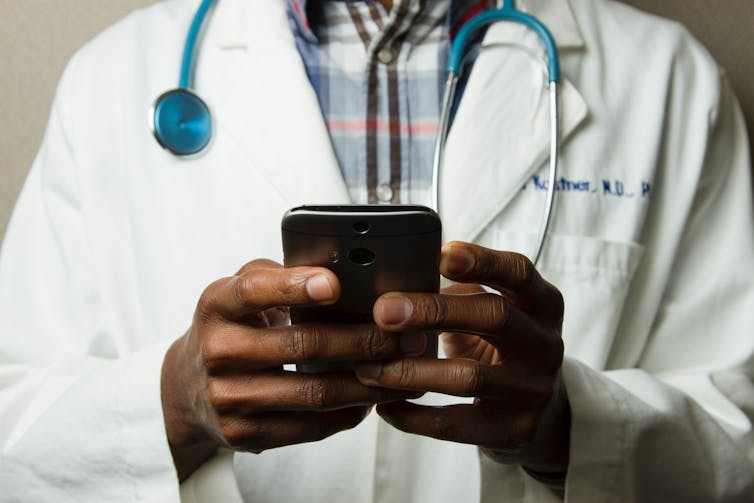 A doctor from the shoulders down looks at a phone and has a stethscope around his neck.