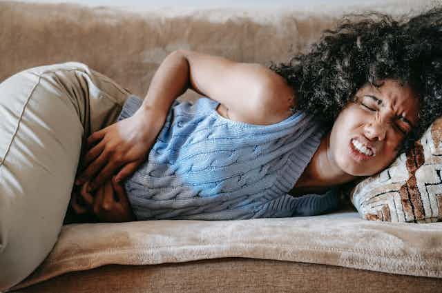 Woman clutching stomach lying on side on sofa