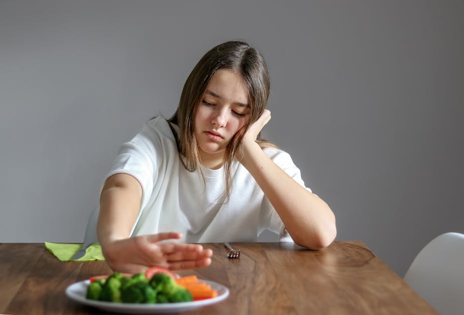 A young girl pushes away a plate of vegetables, refusing to eat.