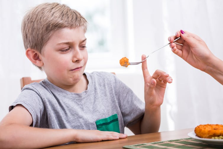 A young boy refuses to eat food from a fork. He looks disgusted.