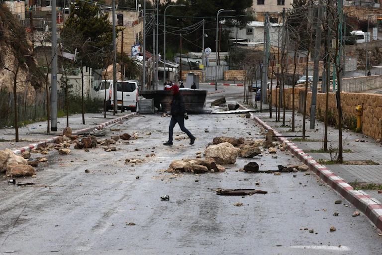 A man crosses a road with improvised road blocks such as rocks.