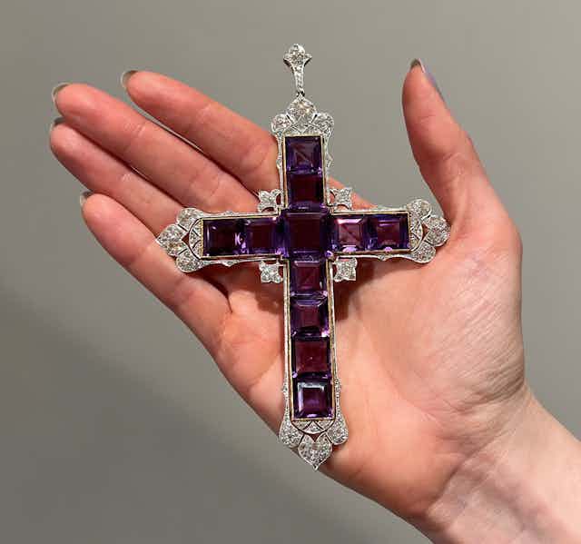 A large palm-sized cross made of purple square jewels and encrusted around the edges with diamonds. 