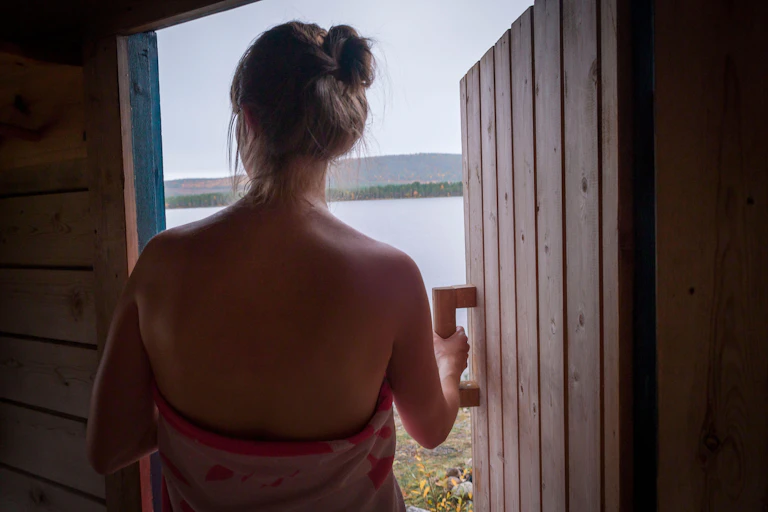 Woman leaves sauna by a lake.