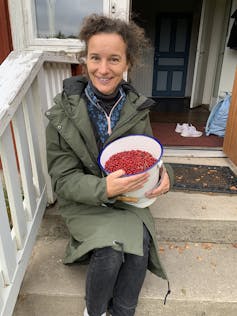 Woman sits holding a bucket of lingonberries.