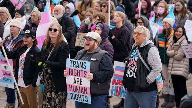A group of people stand together holding signs and symbols of support for transgender people