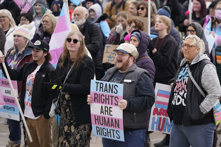 A group of people stand together holding signs and symbols of support for transgender people