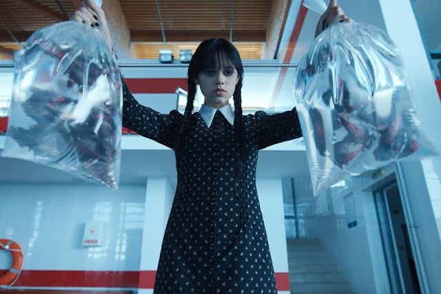 Wednesday Addams holding up two bags of piranhas