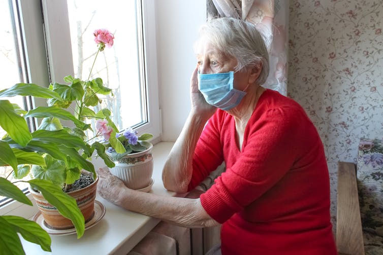 Older woman in mask looks out the window