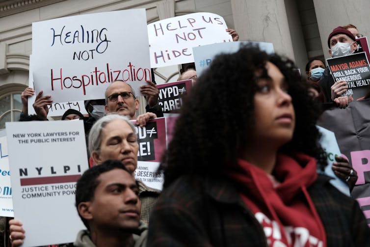 People at a protest hold signs, including one that says 'Healing not Hospitalization'