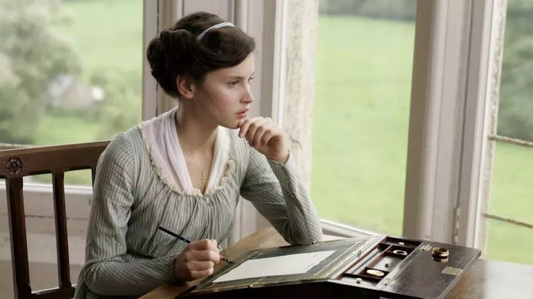 young woman sitting at a writing desk, looking out the window