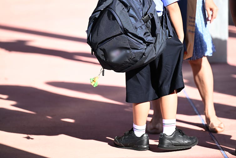 A school child wearing a big backpack with their hand in their pocket.