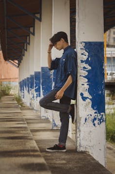 A young man leans against a wall.