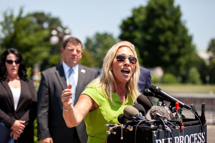 A woman in yellow standing in front of microphones.