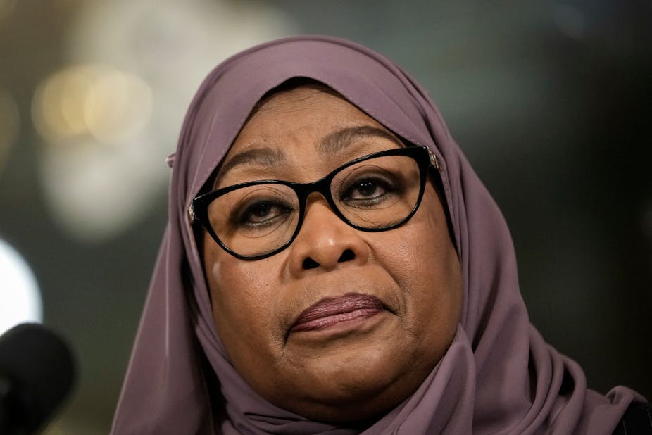 A woman looking ahead, wearing in a deep purple hijab and spectacles.