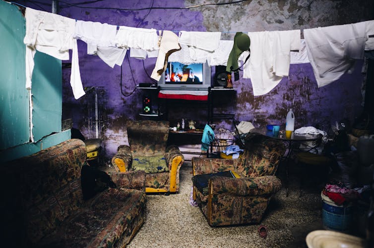 A clothes line hangs above a three piece suite and in front of a television in living quarters in a Centro Habana _albergue_, Cuba, December 2022.