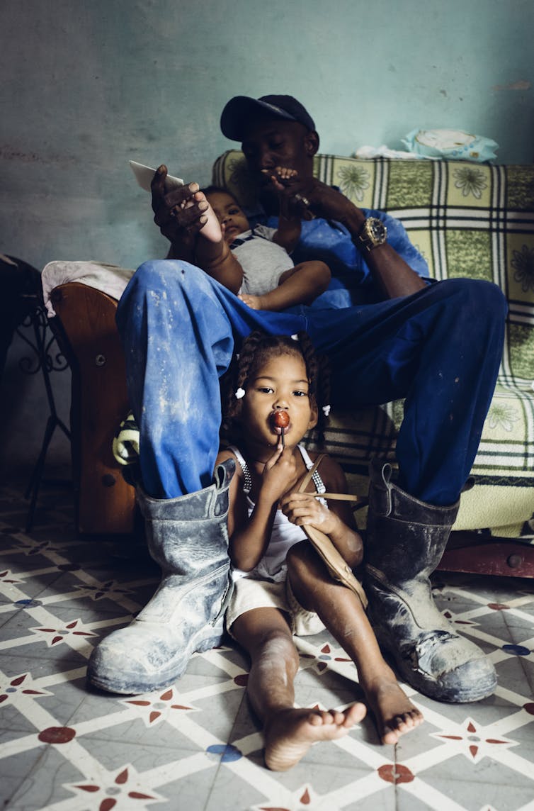 Construction worker Luis Lázaro with Silemis & Sidelaîne, two of his four children sitting on a sofa at home in Havana, Cuba, 2022.