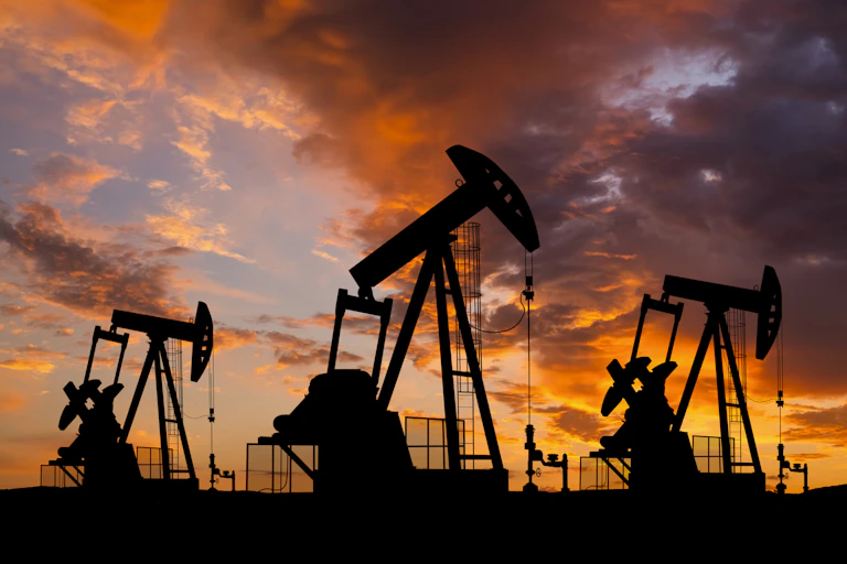 Oil rigs in silhouette against a sky reflecting the setting sun