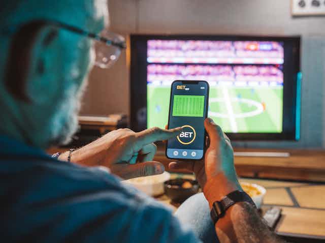 man places bet on smartphone watching game on TV