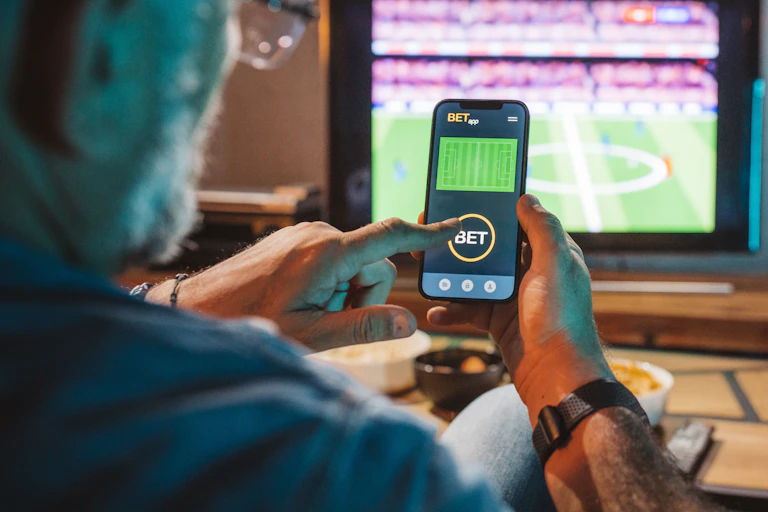man places bet on smartphone watching game on TV
